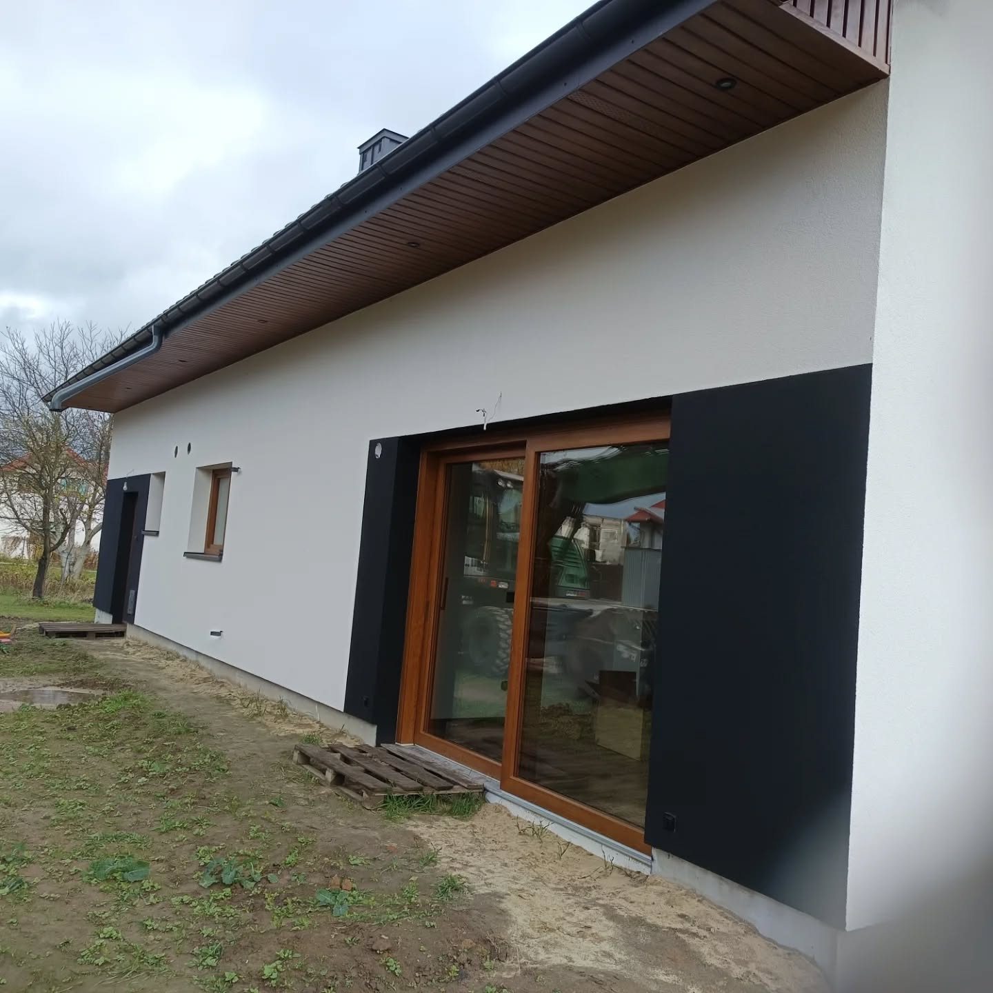 Długa ściana domu z jasną elewacją, brązową podbitką i czarnymi detalami