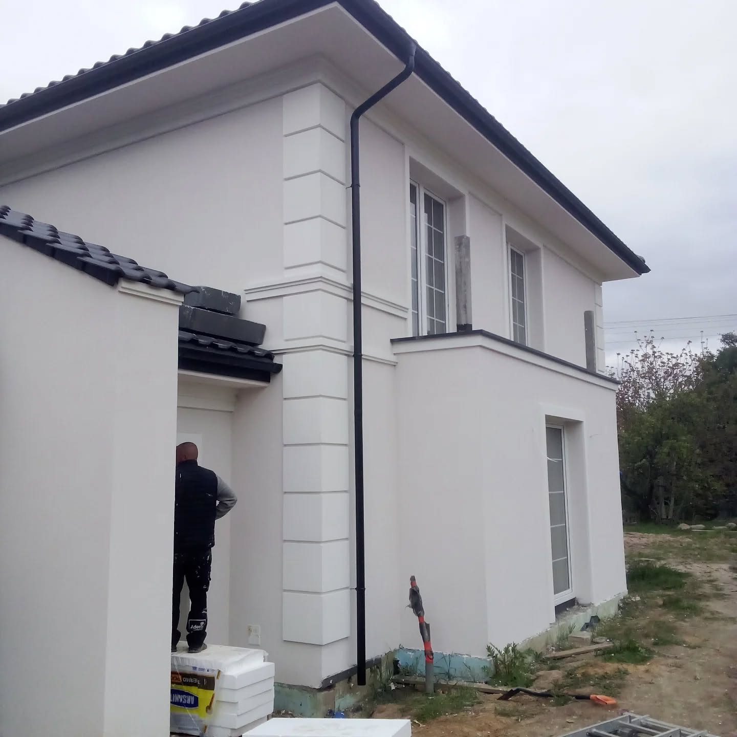 Boczna ściana klasycznego domu z jasną elewacją i czarnymi rynnami