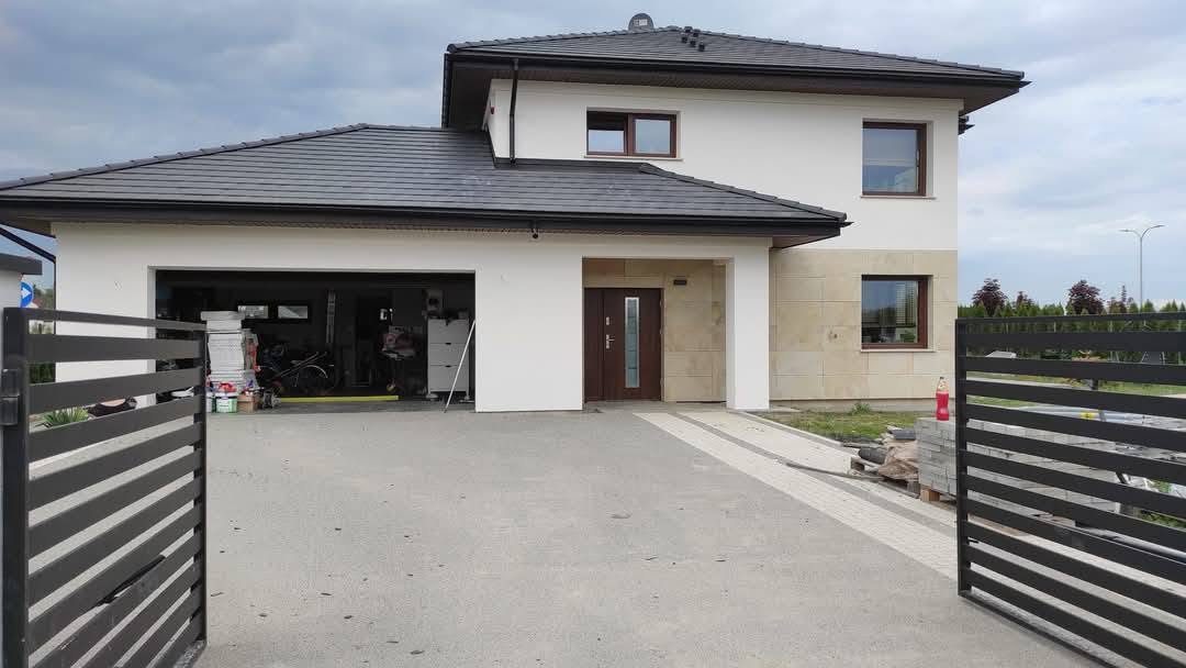 Front domu z jasną elewacją, kamiennym wejściem i czarnym ogrodzeniem